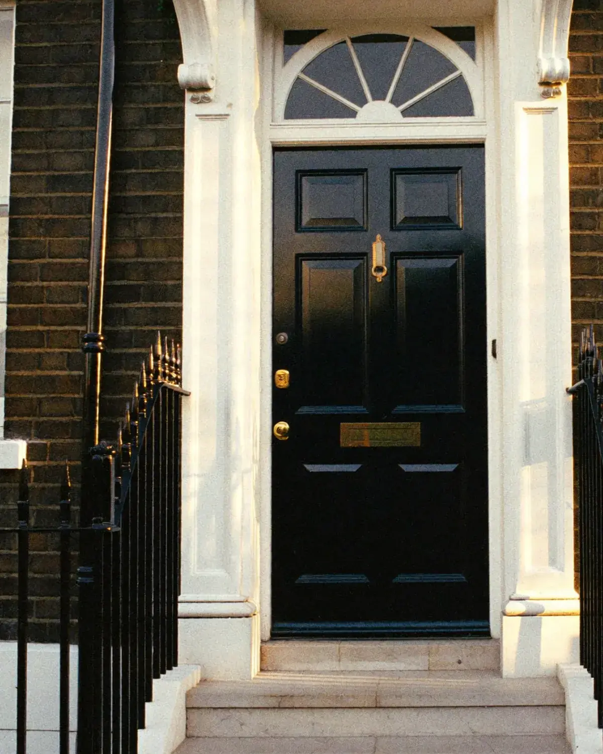 A Georgian terrace doorway in Marylebone — deep navy front door, polished brass, warm morning light