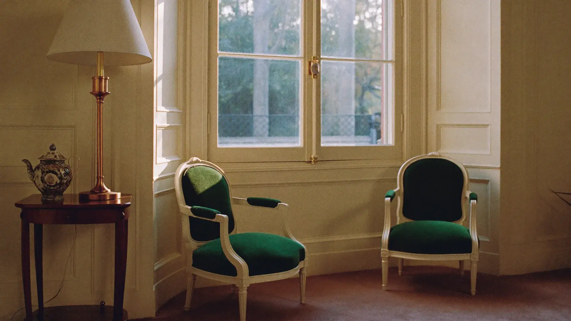 Two deep-green velvet armchairs angled toward each other by a tall window in warm afternoon light