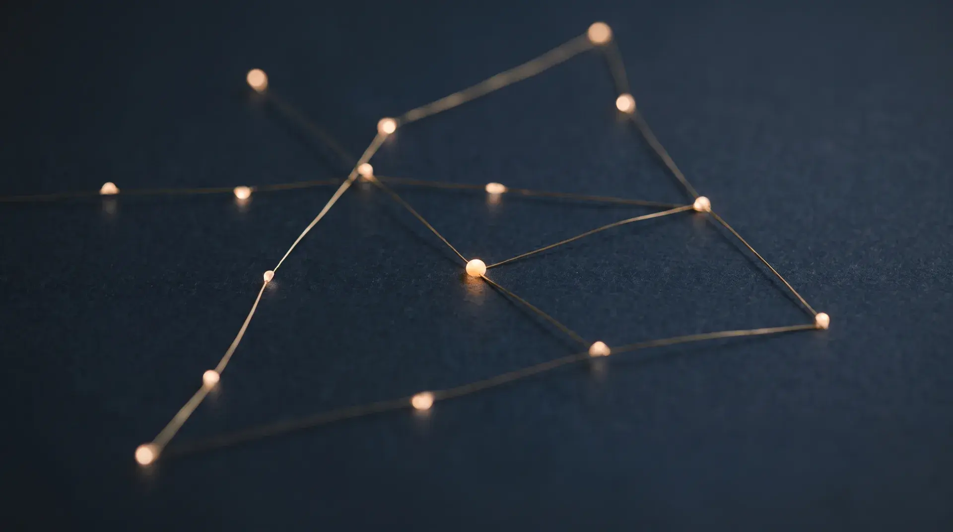 A constellation of warm light points joined by fine brass lines over deep navy, one point brighter than the rest