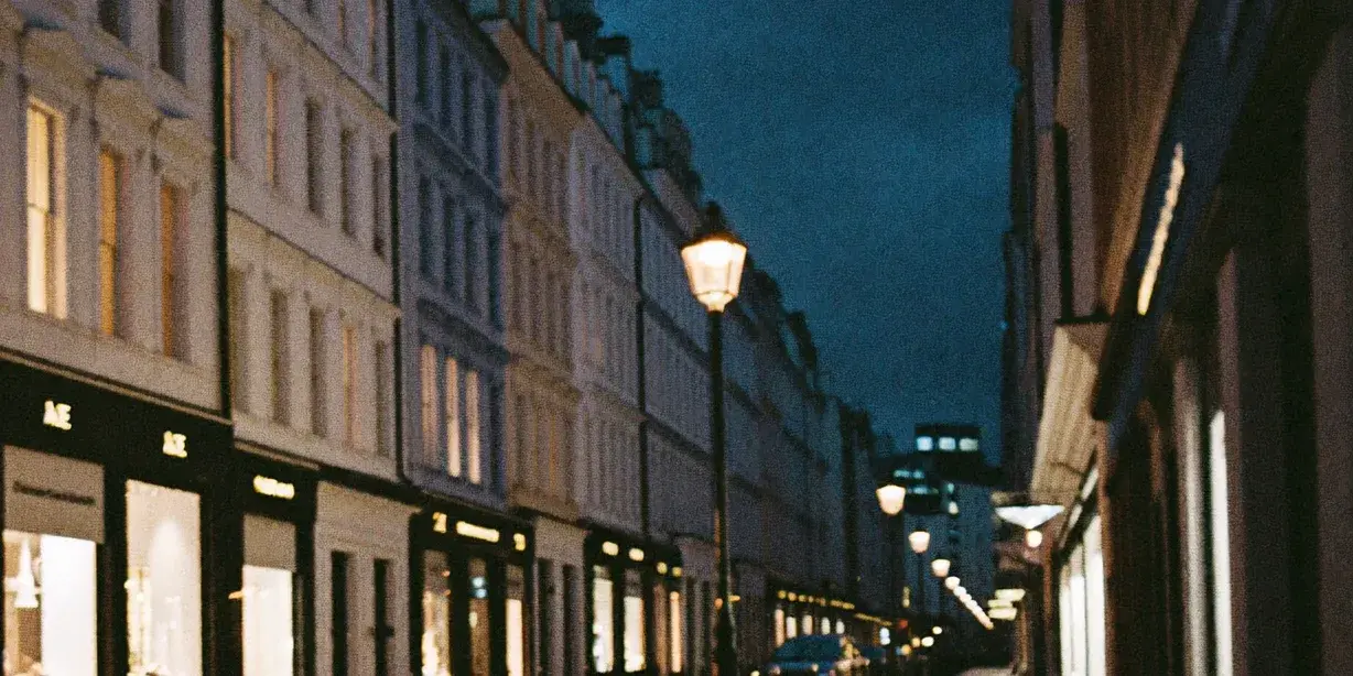 An elegant London shopping street at dusk, warm shop-window light on wet pavement